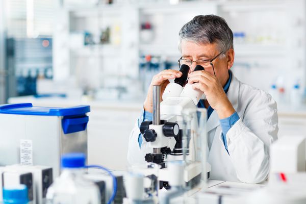 محقق مرد ارشد در حال انجام تحقیقات علمی در آزمایشگاه با استفاده از میکروسکوپ تصویر رنگی کم عمق