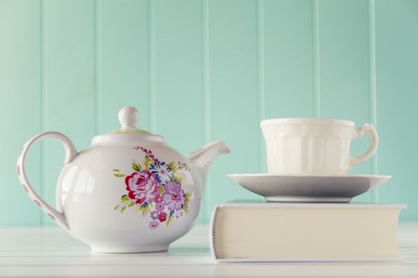 یک قوری و یک فنجان چای روی یک کتاب سفید یک میز چوبی سفید با پس زمینه آبی تخم مرغی سبک وینتیج