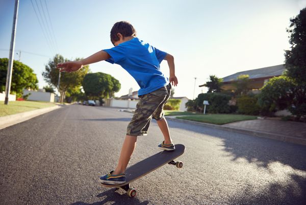 پسر جوانی که در خیابان حومه شهر یاد می‌گیرد اسکیت‌برد سواری می‌کند و سرگرم می‌شود