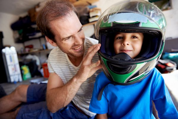 پرتره پسر جوان با کلاه ایمنی پدر و کمک به پدرش در تعمیر موتور سیکلت در گاراژ