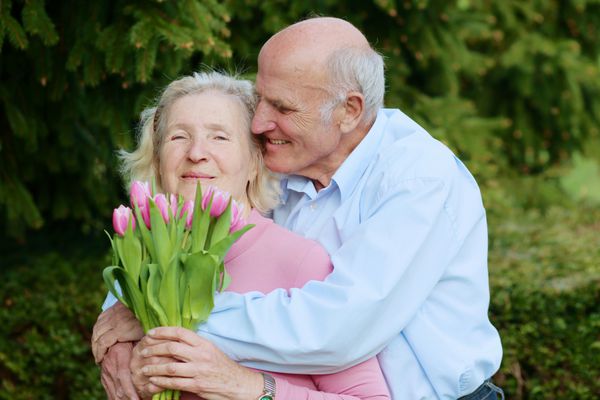 زوج سالمند دلسوز و دوست داشتنی در فضای باز - مردی که دسته گل لاله صورتی را به همسر زیبایش می دهد
