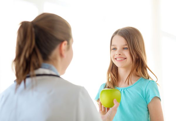 مفهوم مراقبت های بهداشتی کودک و پزشکی - پزشک زن که یک سیب به دختر کوچک خندان می دهد