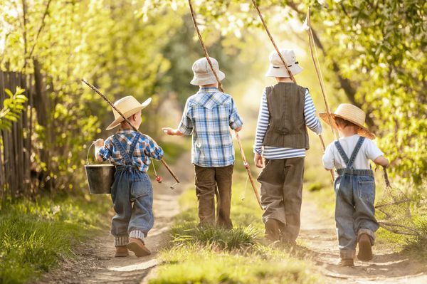 چهار پسر با چوب ماهیگیری در روز آفتابی تابستان به یک سفر ماهیگیری در جاده باریک روستایی می روند
