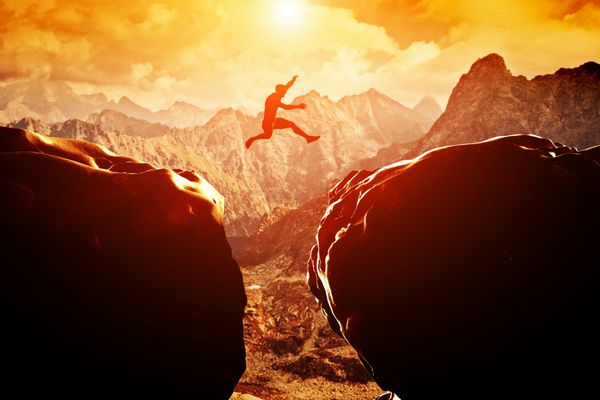 مردی که هنگام غروب آفتاب از روی پرتگاه بین دو کوه می پرد آزادی ریسک چالش موفقیت