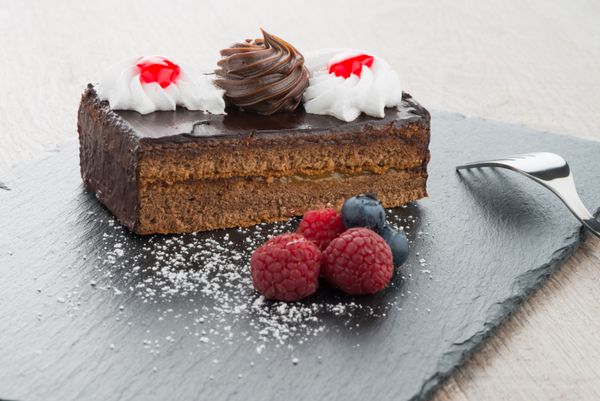 تکه کیک شکلاتی با انواع توت ها در سینی تخته سنگ تیره