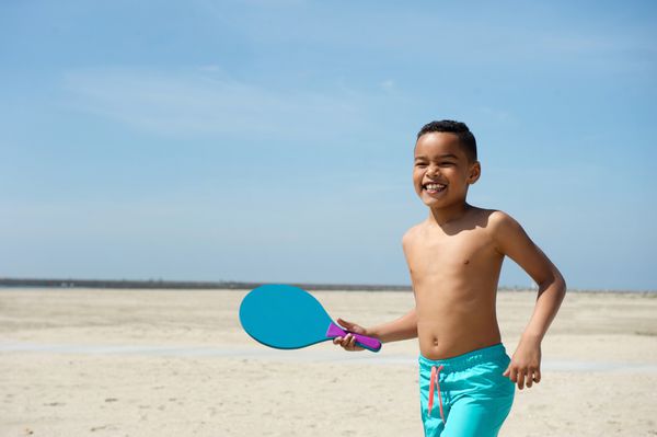 پرتره یک پسر بچه خندان با توپ دست و پا زدن در ساحل