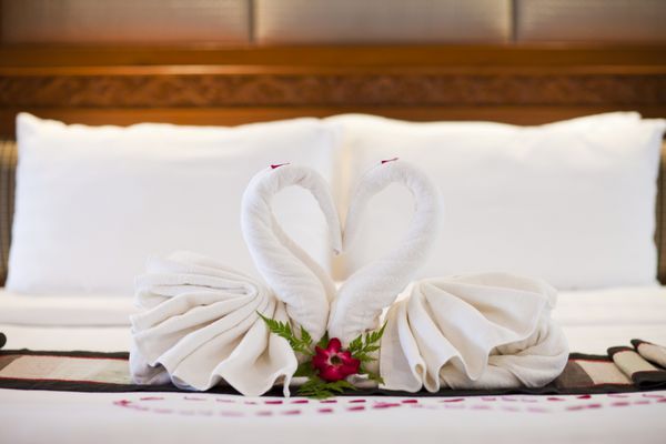 دو قو حوله سفید روی ملحفه تخت گل رز تزئین شده و قلب در اتاق ال