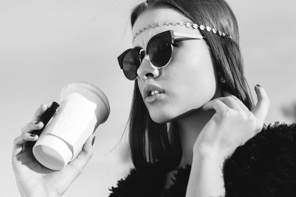 زن هیپستر با عینک آفتابی با فنجان قهوه نمای نزدیک به سبک زندگی سیاه و سفید در فضای باز