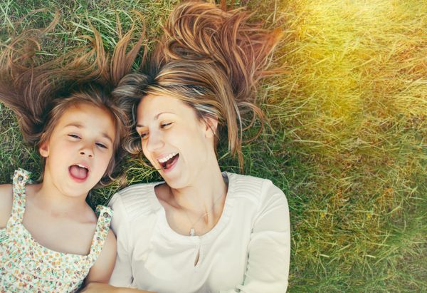 دختر کوچک شاد و مادرش در حال تفریح در فضای باز روی چمن سبز در روز آفتابی تابستان
