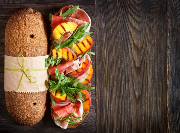 ساندویچ ژامبون خوشمزه با هلو کبابی و آروگولا روی زمینه چوبی با pl برای متن