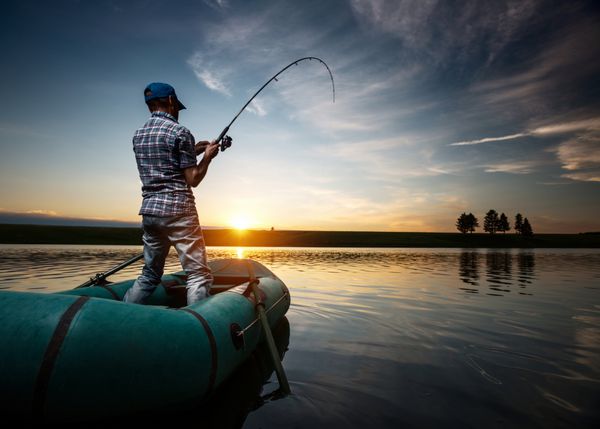 مرد بالغی که در غروب آفتاب از قایق روی برکه ماهیگیری می کند