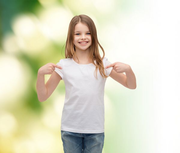مفهوم طراحی تی شرت - دختر کوچک خندان در تی شرت سفید خالی که به سمت خودش اشاره می کند