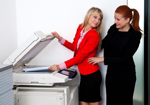 دو همکار زن جذاب تجاری که روی چاپگر اداری و چت کار می کنند