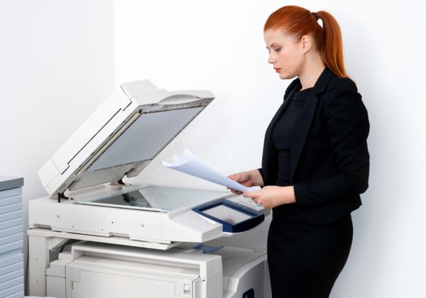 زن تاجر مو قرمز جذاب که روی دستگاه چاپگر اداری کار می کند