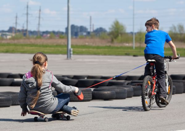 دختر جوان روی اسکیت برد پسر کوچکی را با دوچرخه در پیست ورزشی دنبال می کند
