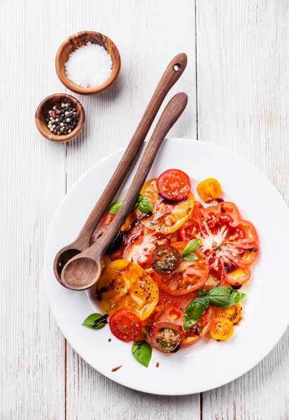سالاد گوجه فرنگی رنگارنگ تازه رسیده با روغن زیتون و سرکه بالزامیک در زمینه چوبی سفید