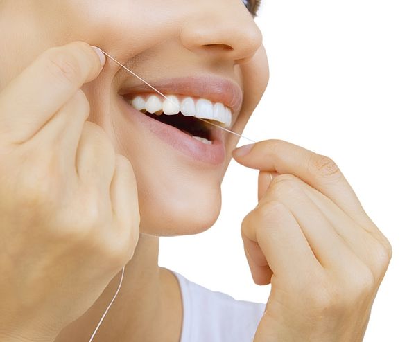 نخ دندان زن و دندان - زن جوان قفقازی در حال نخ دندان کشیدن لبخند زن از نمای نزدیک
