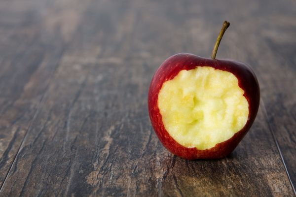 سیب قرمز با سوراخی که در آن روی موج‌سواری چوبی قهوه‌ای گزیده شده است