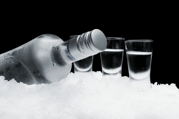 نمای نزدیک بطری با لیوان های ایستاده روی یخ روی مشکی