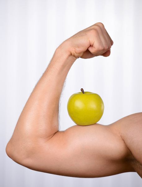 سبک زندگی سالم تصویر برش خورده مرد عضلانی که عضله دوسر کامل خود را با یک سیب سبز روی آن نشان می دهد