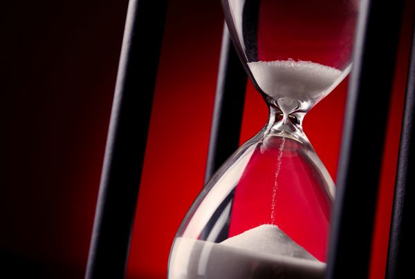 تایمر تخم مرغ یا ساعت شنی روی پس زمینه قرمز مدرج در تصویر مفهومی از گذر زمان و مدیریت زمان