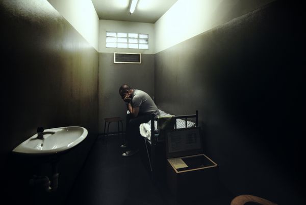 مردی در اتاق کوچکی از زندان تاریک روی تخت نشسته است