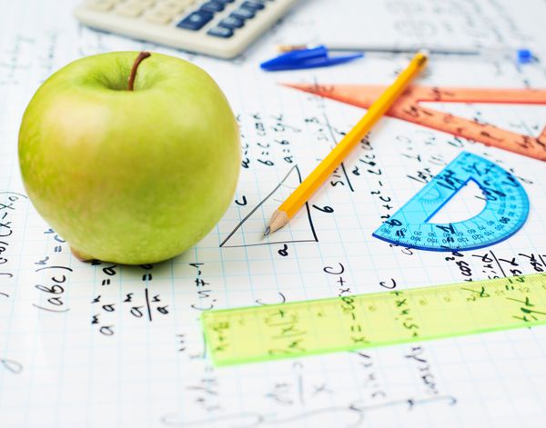 مطالعه ریاضی از بازگشت به مدرسه ترکیب سیب سبز و تعدادی لوازم التحریر دفتری که روی برگه پر از معادلات و فرمول های مثلثاتی قرار گرفته است