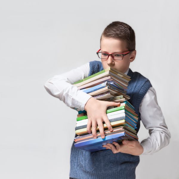 نوجوان دانش‌آموز باهوش با عینک دسته‌ای از کتاب‌ها را در دست دارد