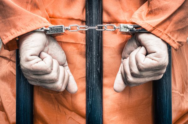 دستان دستبند شده یک زندانی پشت زندان با لباس های نارنجی - نگاه فیلتر شده دراماتیک ترد و غیراشباع
