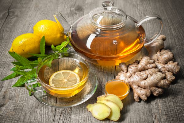 فنجان چای زنجبیل با عسل و لیمو روی میز چوبی