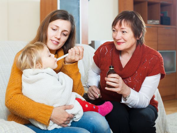 زن جوان با مادری بالغ که در خانه به کودک نوپا شربت دارویی می دهد