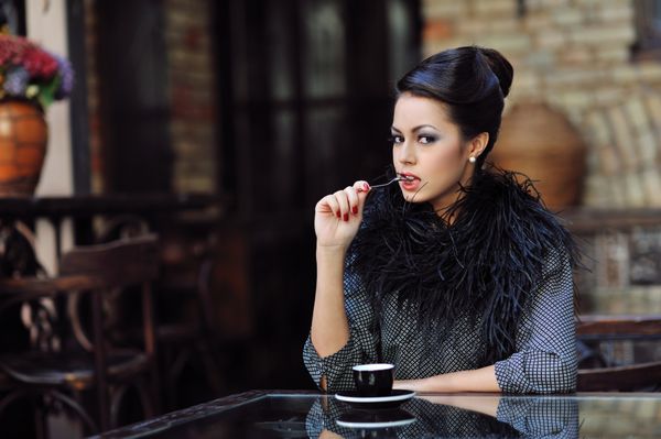 زن جوان زیبا با یک فنجان قهوه در کافه نشسته است
