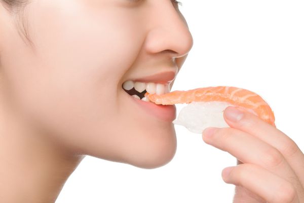 زن جوان در حال خوردن سوشی ماهی قزل آلا با دست جدا شده در پس زمینه سفید
