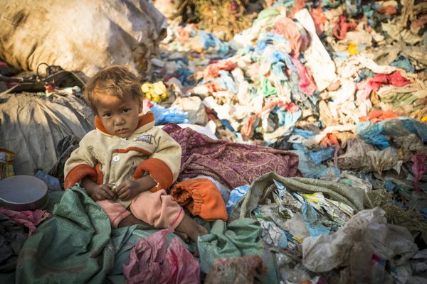 کاتماندو نپال - 22 دسامبر 2013 کودک ناشناس نشسته است در حالی که والدینش در حال کار بر روی زباله هستند در نپال 50000 کودک در 60 درصد موارد به دلیل سوء تغذیه جان خود را از دست می دهند