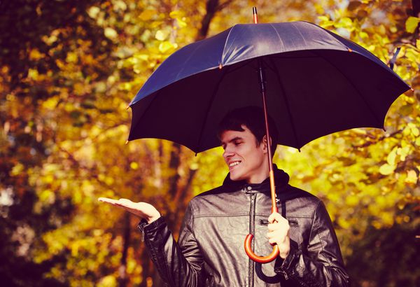 مرد جوانی که در روز پاییز چتر در دست دارد