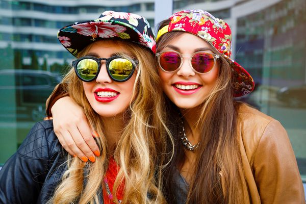پرتره مد از نزدیک از دو دختر زیبا با کت‌های چرمی که کلاه‌های خود را به تن دارند و عینک‌های آفتابی آینه‌ای دارند دارای e و موهایشان و لب‌های درخشان هستند بهترین دوستان پرتره مثبت