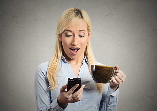 پرتره نزدیک زن خندان و شاد کسب و کار در حال خواندن خبرهای خوب در تلفن هوشمند وکیلی که پس‌زمینه خاکستری جدا شده از فنجان قهوه را در دست دارد بیان احساسات مدیران شرکت