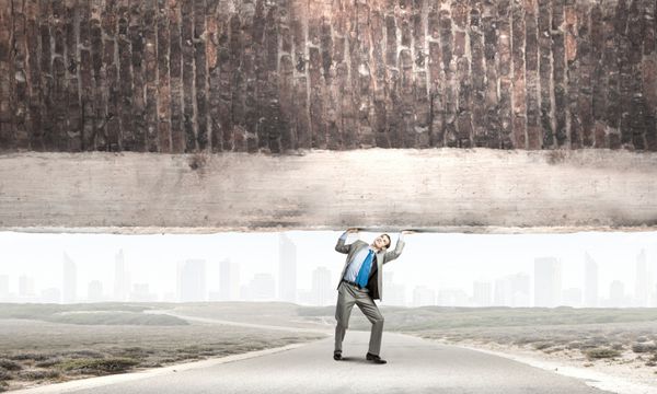 تاجر جوان قدرتمند در حال بلند کردن دیوار آجری بالای سر