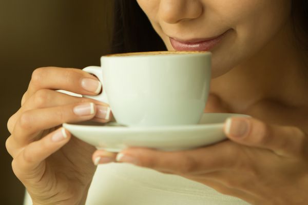 قهوه دختر زیبا در حال نوشیدن چای یا قهوه در کافه زن مدل زیبایی با فنجان نوشیدنی رنگ های گرم تنیده