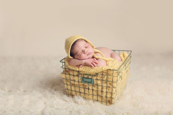 نوزادی که کلاه زرد بر سر دارد و در یک سبد روی یک پتوی زرد خوابیده است