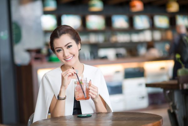 زن زیبا در حال نوشیدن نوشیدنی شیرین در کافه
