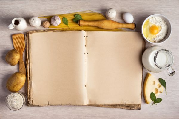 کتاب آشپزی قدیمی و مواد لازم برای دستور غذا در یک قاب در پس زمینه میز