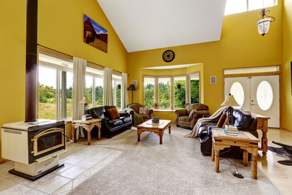 خانه لوکس زیبا با سقف طاقدار بلند و دیوارهای زرد روشن اتاق خانوادگی بزرگ با نیمکت های چرمی میزهای چوبی و اجاق گاز عتیقه