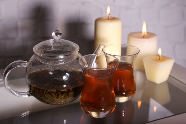 ترکیب با چای در قوری شیشه ای و شمع روی میز در پس زمینه روشن