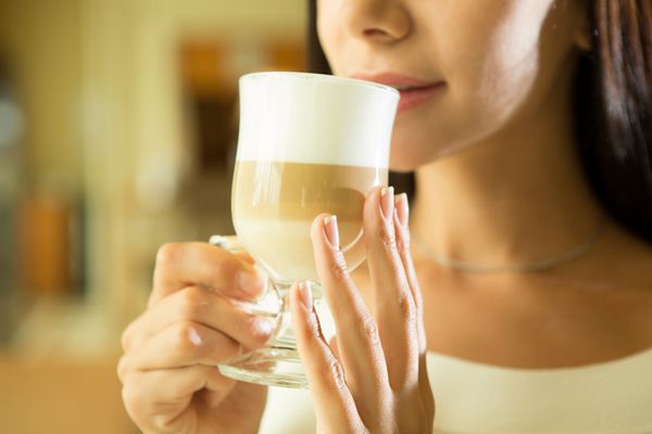 قهوه دختر زیبا در حال نوشیدن چای یا قهوه در کافه زن مدل زیبایی با فنجان نوشیدنی رنگ های گرم تنیده