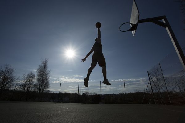 سیلوئت یک بسکتبالیست در هوا در زمین بسکتبال در فضای باز که در یک روز آفتابی روشن در حال کوبیدن است تاری حرکت