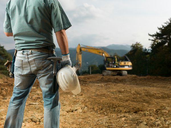 نمای پشت مهندس مرد ایستاده در محل ساخت و ساز و کلاه سفید را در دست دارد