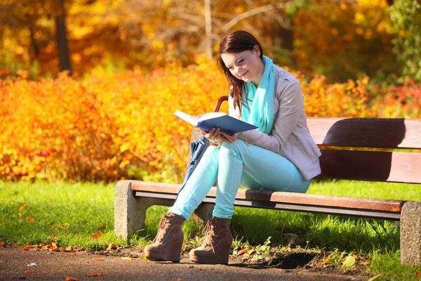 مفهوم سبک زندگی پاییزی دختر جوان در حال استراحت در پارک پاییزی در حال خواندن کتاب پس زمینه برگ های رنگارنگ طلایی