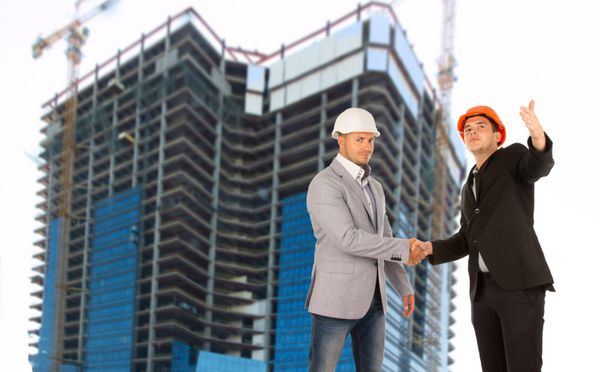 معمار و مهندس سازه در حال دست دادن در یک سایت ساختمانی زیر یک ساختمان مدرن بلند در حال ساخت در حالی که به یکدیگر تبریک می گویند یا توافق نامه و مشارکت را امضا می کنند