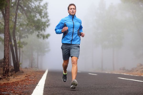 تمرین مرد دونده سالم در جاده کوهستانی مدل تناسب اندام مردانه دویدن در حال تمرین برای ماراتن در جاده جنگلی در منظره طبیعت شگفت انگیز